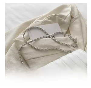 Detail of white quilted crossbody bag with rhinestone buckle and chain strap on a blazer