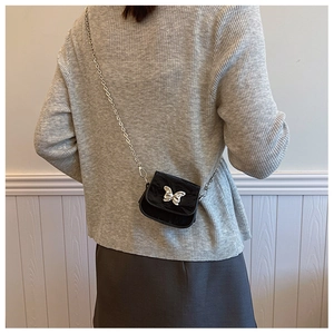 Vue arrière d'un mini sac noir avec chaîne et papillon argenté sur un pull gris