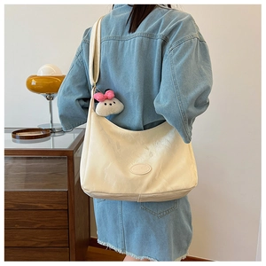Detail of off-white hobo bag with soft pleated texture and cute plush pendant