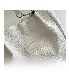Close-up of white woven texture and oval leather logo on a large tote handbag