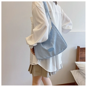 Detail of light blue crossbody dumpling bag showing pleated fabric texture and logo
