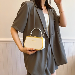 White mini box crossbody bag with gold metal trim and chain strap shown on a gray suit