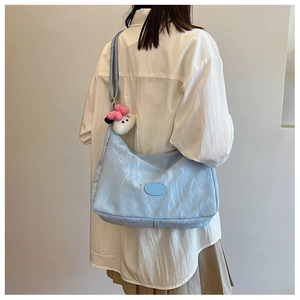 Detail of light blue pleated dumpling bag with cute plush pendant and soft texture finish