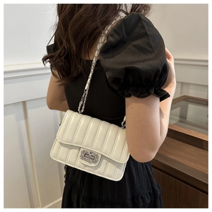 White quilted shoulder bag with silver chain and rhinestone lock on black dress