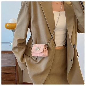 Vue détaillée du mini sac rose à chaîne avec fermoir papillon argenté sur un tailleur