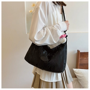 Detail of black crescent shoulder bag with a plush character pendant and wrinkled texture