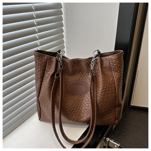 Detail of brown woven tote bag featuring silver chain strap and oval leather brand logo