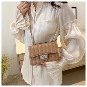 Detail of beige quilted crossbody bag featuring a sparkling rhinestone turn-lock closure