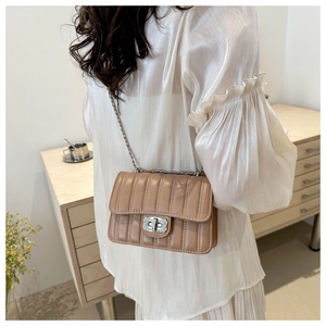 Close-up of quilted light brown shoulder bag with rhinestone buckle on cream top