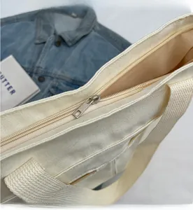 Detailed close-up of smooth metal zipper and reinforced handle on a cream canvas tote bag