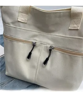 Close-up of off-white canvas tote bag featuring double zippers and durable textured fabric