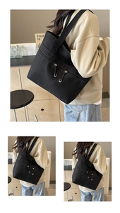 Detail of black canvas tote bag showing front double parallel zipper pockets and strap