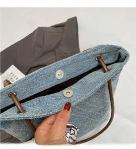 Dettaglio della borsa denim con chiusura magnetica argento e manico in pelle marrone