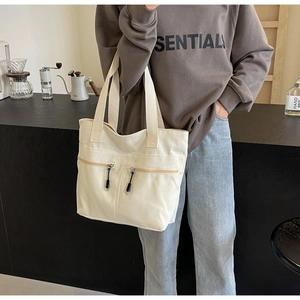 Close-up of cream canvas tote bag featuring unique dual front zipper pockets and black pulls