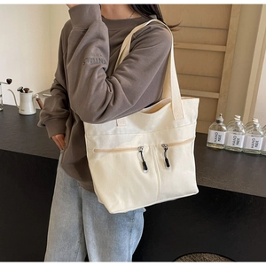 Side view of beige canvas tote bag with front zip pockets worn by model