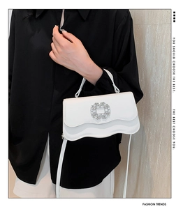 Close-up of white leather handbag featuring wavy flap design and square rhinestone buckle