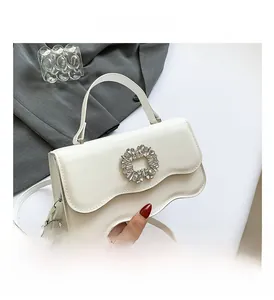Detailed close-up of a white textured crossbody bag featuring a large square rhinestone buckle