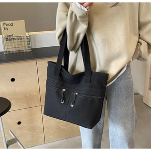 Detail of black canvas tote bag showing dual front metal zipper pockets and large capacity