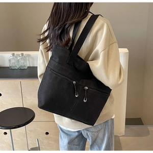 Detail of minimalist black canvas tote bag showing double zip front pockets and wide strap