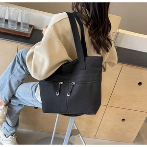 Detail view of black canvas tote bag with dual zipper pockets and wide shoulder straps