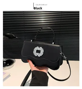 Detail of black crossbody bag featuring sunflower rhinestone buckle and wavy flap design