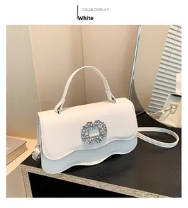 Detail view of white leather crossbody bag featuring a sparkling rhinestone floral buckle
