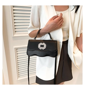 Detailed close-up of a black leather bag with wavy flap and sparkling crystal buckle
