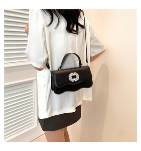 Detail shot of black leather shoulder bag with rhinestone buckle on wave edge flap