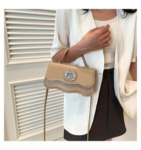 Detail of elegant beige crossbody bag featuring a wavy flap and sparkling crystal buckle