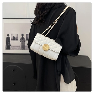Detail view of white quilted crossbody bag with gold round lock and chain strap on model