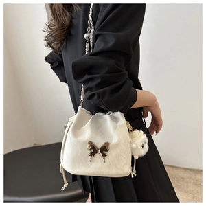 Detail of a beige drawstring bucket bag with silver butterfly relief and plush lamb charm