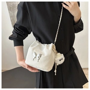 Detail of white drawstring bucket bag with silver butterfly charm and plush monster pendant