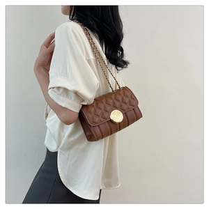 Detailed close-up of dark brown quilted mini crossbody bag with gold chain strap on a model