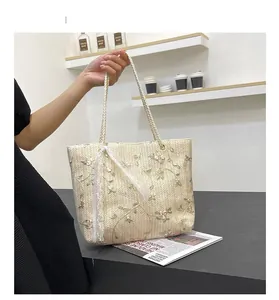 Detail of beige straw tote bag with delicate floral embroidery and white lace ribbon