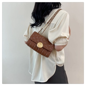 Detail of a brown quilted crossbody bag featuring a large gold spiral textured buckle