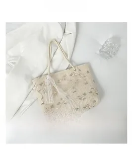 Detail of beige straw tote bag with floral embroidery and white lace tassel charm