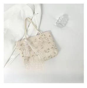 Detail of beige straw tote bag featuring delicate floral embroidery and lace ribbon