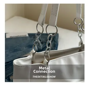 Dettaglio della catena d'argento e dell'anello metallico sulla borsa a spalla bianca