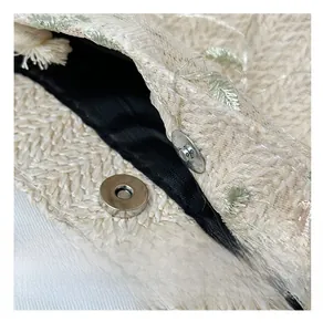 Detail of silver magnetic buckle and lace embroidery on straw shoulder tote bag