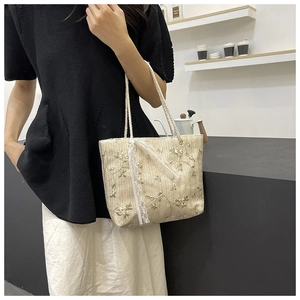 Detail of hand-woven straw tote bag with delicate green floral embroidery and white lace bow