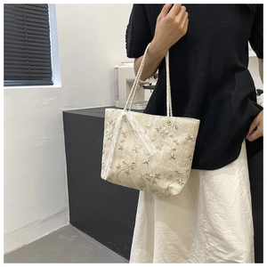 Detail of cream straw tote bag with delicate green floral embroidery and lace ribbon bow