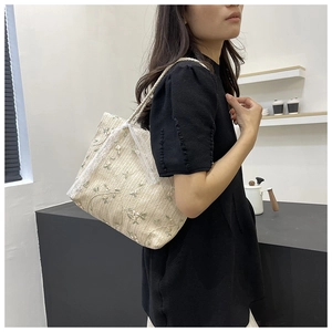 Detail of straw tote bag with floral embroidery and lace ribbon bow on a shoulder