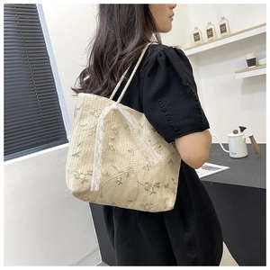 Close-up of woven straw tote bag with delicate floral embroidery and white lace bow detail