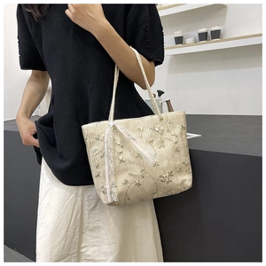 Close-up of straw tote bag with floral embroidery and white lace bow detail