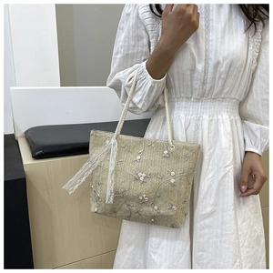 Close-up of straw tote bag featuring white floral embroidery and delicate lace details