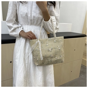 Detail of floral embroidery and white lace bow on green straw tote bag for summer