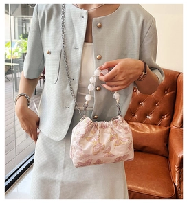 Detail of pink satin bucket bag featuring gold butterfly embroidery and pearl handle