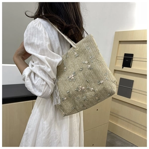 Detail of straw tote bag featuring floral embroidery and white lace trim on the side