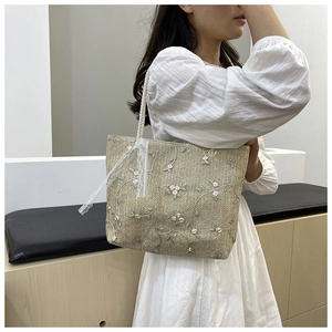 Detailed close-up of straw tote bag featuring floral embroidery and white lace ribbon