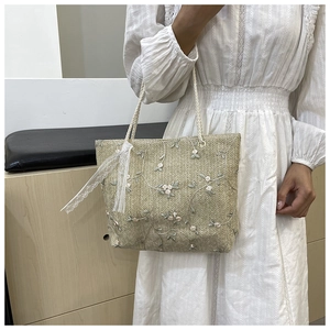 Close-up of women's straw tote bag featuring delicate floral embroidery and lace trim